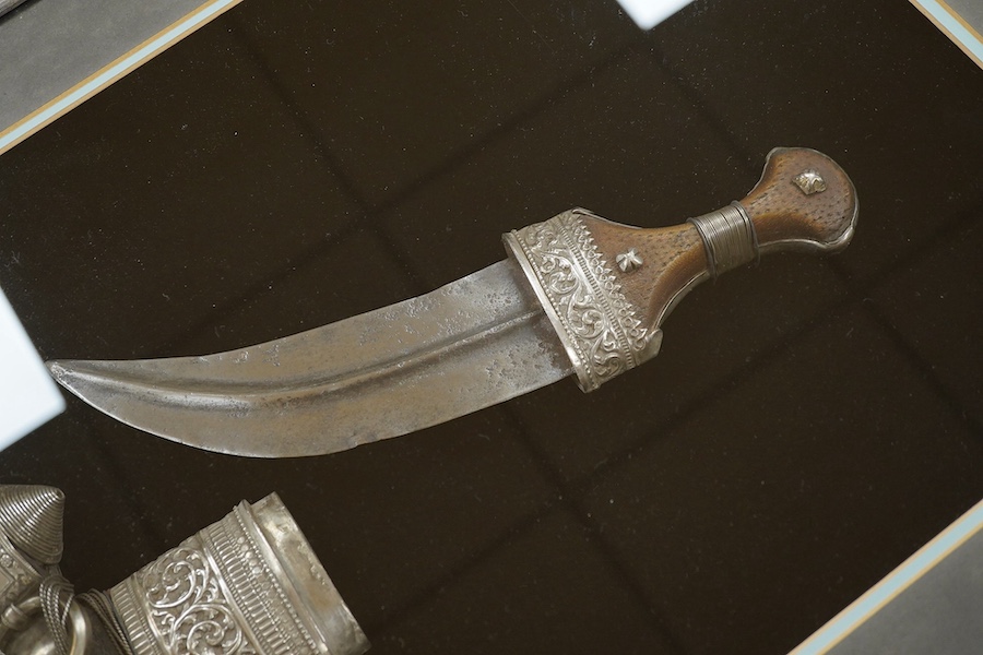 A silver mounted Arab Khanjar dagger from Oman, wooden grip, mounts chased in relief with scrolling foliage, contained in an illuminated display case for wall mounting, 79cm x 58.5cm. Condition - good.